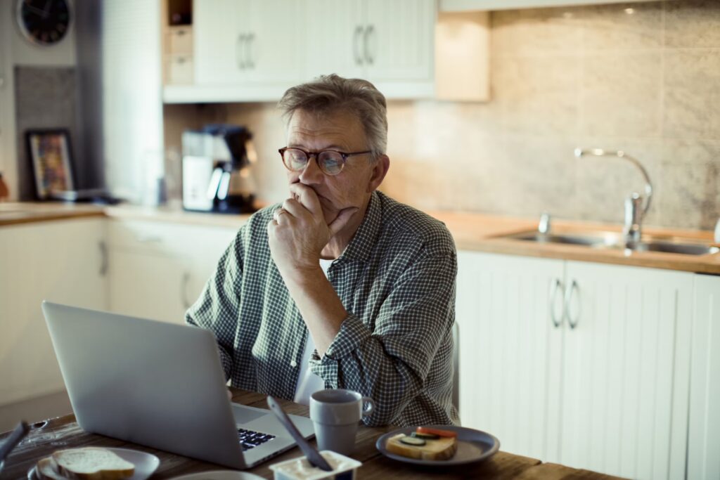 Close up of a mature man using a laptop at home while having breakfast